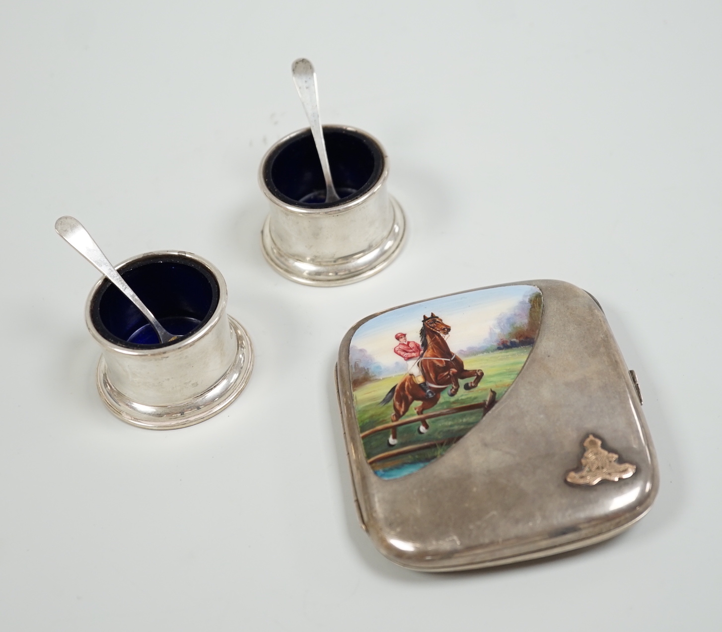 An Edwardian silver and enamel cigarette case, decoration with horse and jockey leaping a fence, import marks for Birmingham, 1908, 96mm, with military applique and inscription and a pair of Birks sterling condiments.